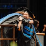 Rachel Perkins hugs a faculty member on the commencement stage.